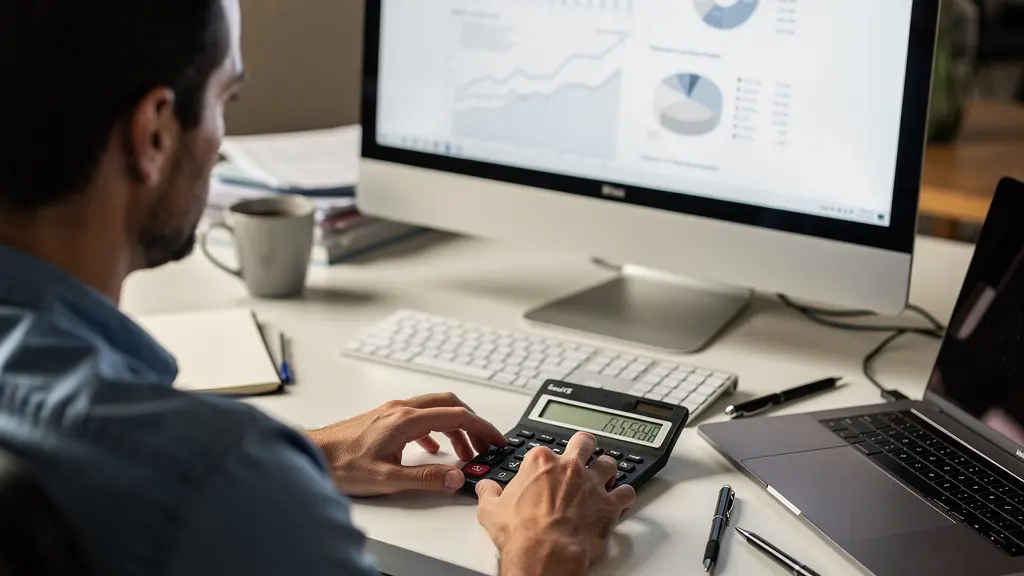 Personne comparant des frais de courtage sur une calculatrice devant un écran